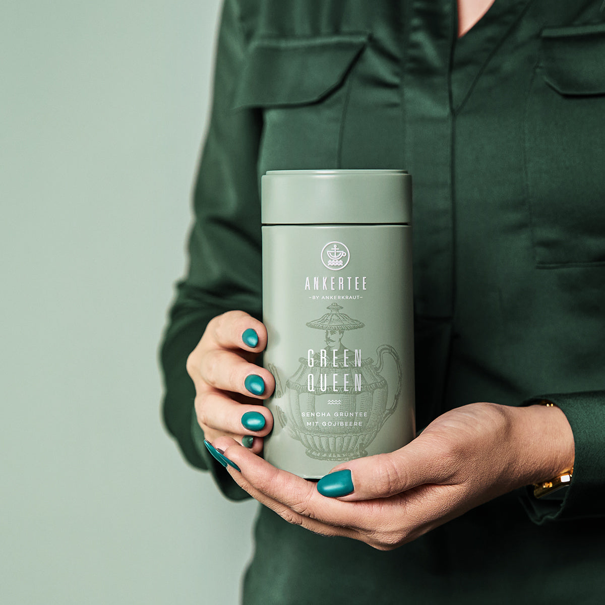 Eine Frau mit grüner Bluse hält in ihren Händen eine Ankertee-Dose mit der Aufschrift GREEN QUEEN.