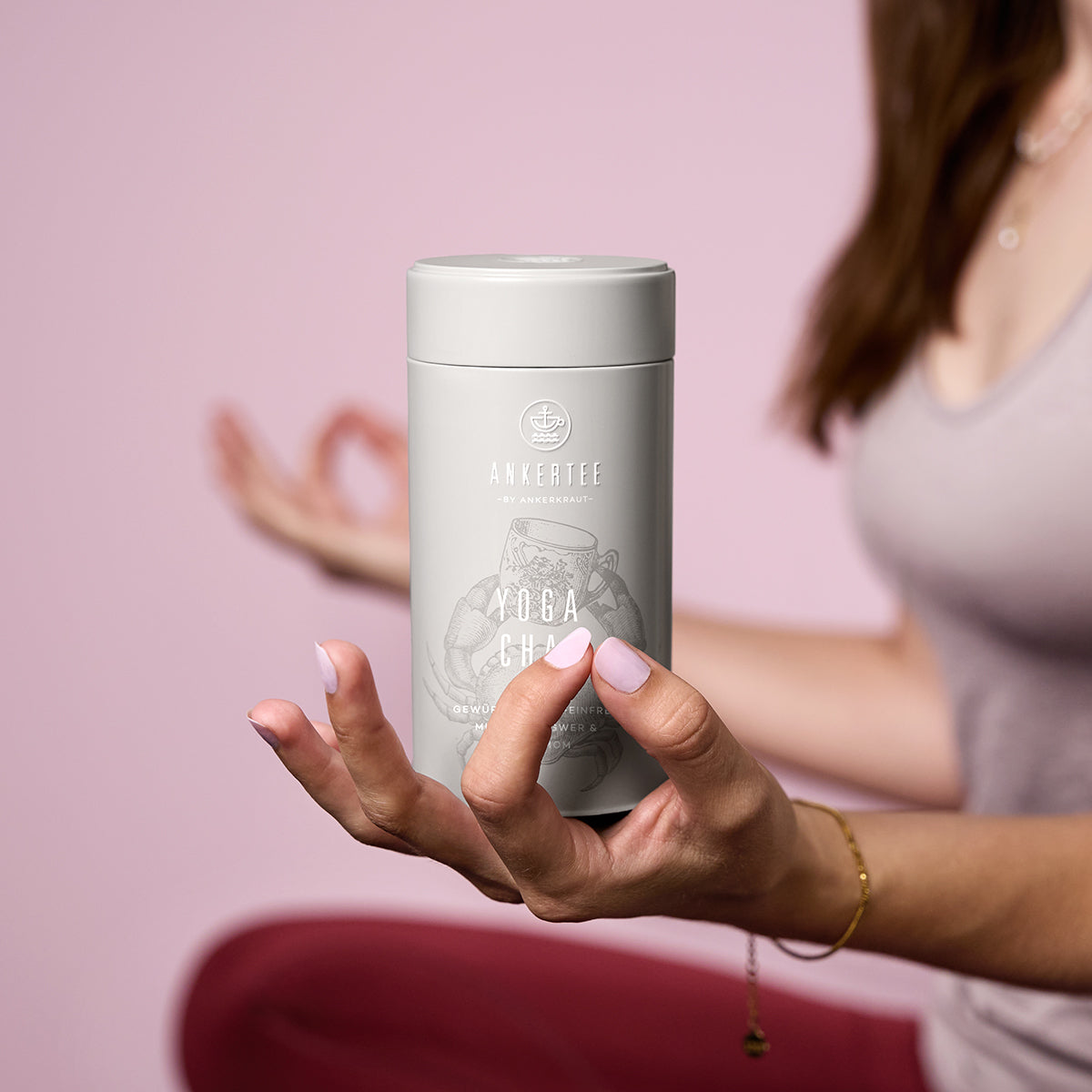 Eine Frau in Yoga-Sitzhaltung hält eine Ankertee-Dose mit der Aufschrift YOGA CHAI